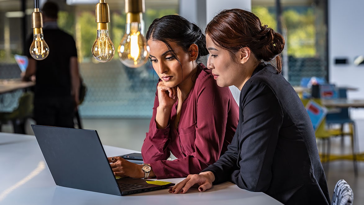 Two women work on laptop together at desk