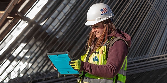 A woman wearing safety gear working on a construction site and using a tablet