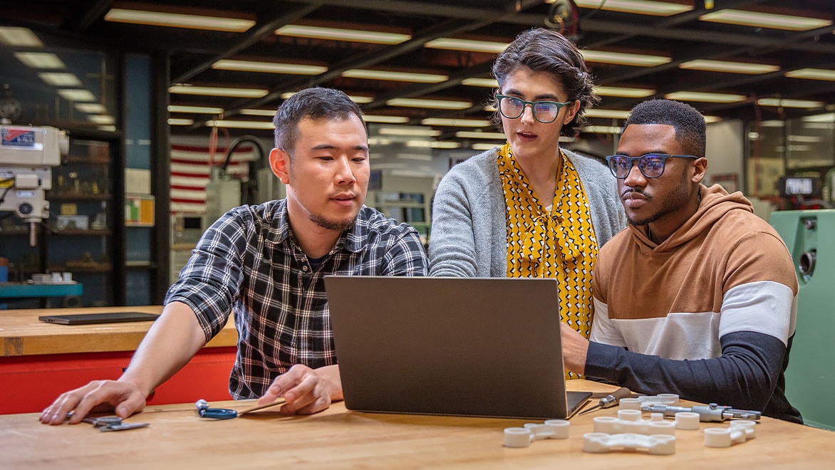 Woman points to laptop screen while speaking to two men viewing the screen