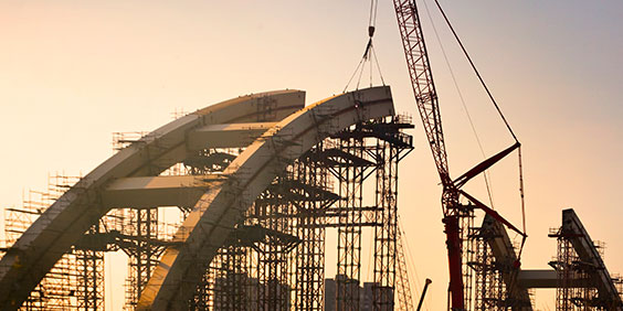 A half-built concrete arc supported by scaffolding with a crane in the background