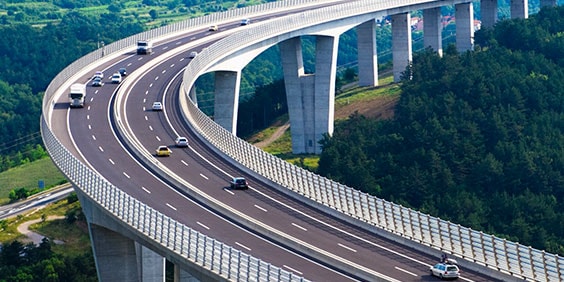 Curved highway with light vehicle traffic surrounded by trees and rolling hills