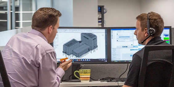 2 men sitting in front of 2 computer monitors with a black-and-white building model displayed on 1 of the screens