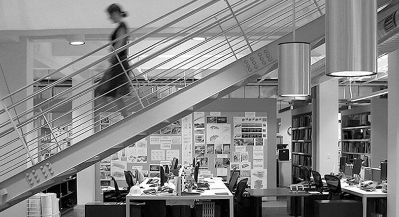 Grayscale photograph of an office with a woman walking down a flight of stairs